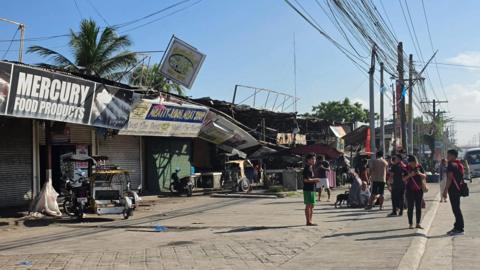 People standing beside damaged buildings in southern Philippines after an earthquake