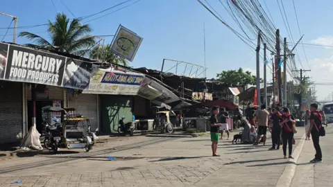 People standing beside damaged buildings in southern Philippines after an earthquake