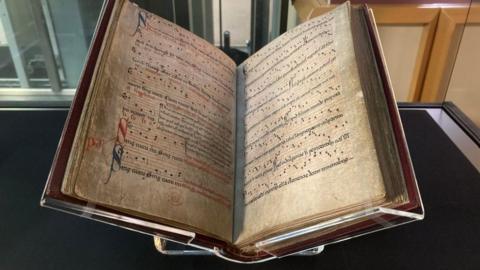 Manuscript printed with medieval English music behind a glass case in a museum.