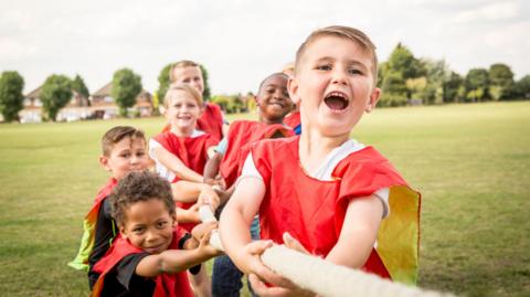 Children wearing red bibs playing tug of war in a field