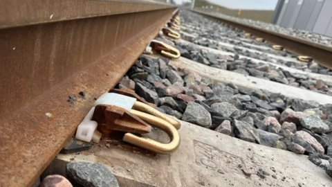 Close-up image of metal railway tracks, metal bolt fasteners, concrete supports and large pieces of gravel.