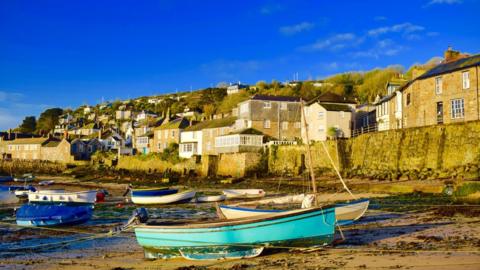 bright blue sky behind houses on a hill leading to an inlet and boats in the foreground 