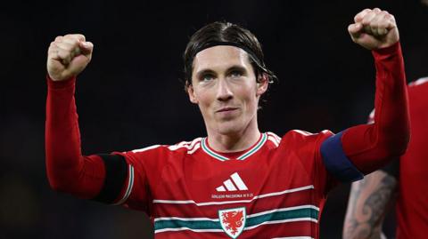 Harry Wilson celebrating with both arms raised while in red Wales kit