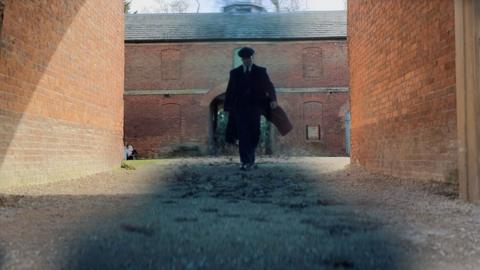 A composite image of Cillian Murphy as Tommy Shelby walking through a courtyard in the new Peaky Blinders Film, with a lighter image of the courtyard in the daylight.