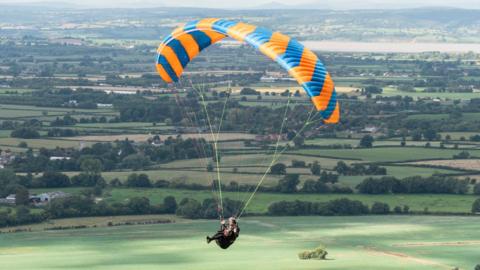 A paraglider flies over English countryside.