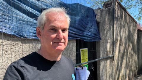 David Redman wearing a black T-shirt and standing in front of the works site in Torquay