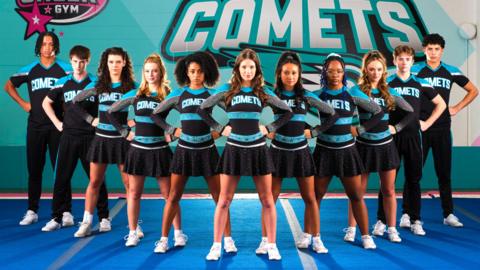 cheerleaders standing in a line wearing blue and black cheer kit