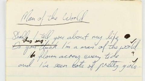 A close up image of a yellowed piece of lined paper with scrawled blue writing upon it which reads: "Man of the world." 