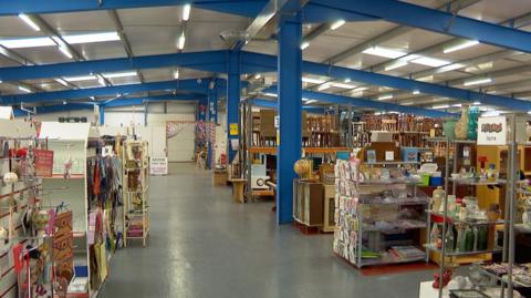 The Acorn shop is in a large modern building. There are many shelving units holding vases, clothes, books and furniture.