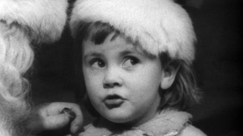 A close up of a little girl in a Santa hat telling Father Christmas what she wants.