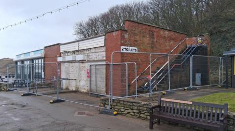 A public toilet block located on the seaside is closed and fenced off. 