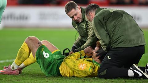 Josh Sargent, lying on the pitch, receives treatment from the Norwich City medical staff during their game with Sheffield United