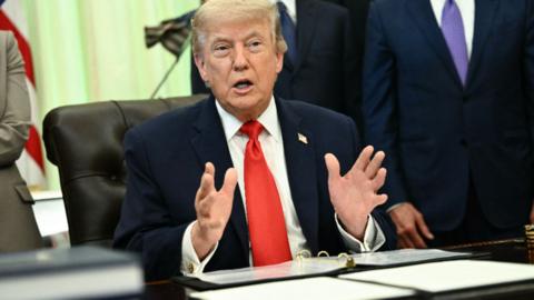 Donald Trump sat behind a desk with his hands out in front of of him.