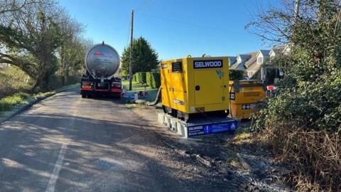 Machinery and large vehicles are parked by the side of a country road.