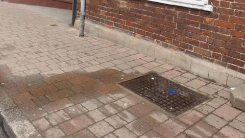 A manhole cover on a pavement, with a damp patch coming from it