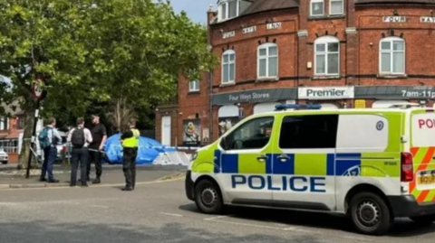 A police van is parked up in Walsall with officers talking to people in the street near a police cordon
