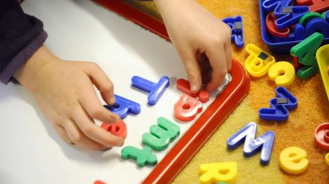 A child playing with a magnetic board with multicoloured letters.