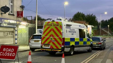 Police van at crash scene with road closed sign