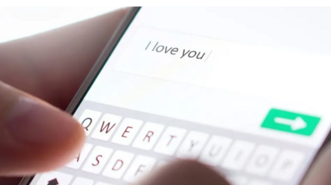 A phone screen with 'I love you' typed out on the screen. A hand appears to be holding the phone. 