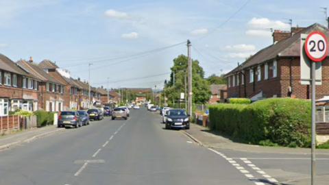 A street view of Stanley Grove. It is a main road lined with houses and cars parked on the pavement.