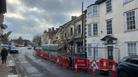 A kebab shop being propped up by wooden scaffolding on Northgate Street in Devizes following a fire. In front of the shop are red and white safety barriers and cones and a metal fence