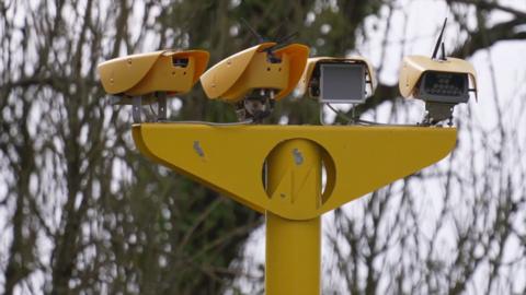 A close-up of a bright yellow speed camera with an array of four sensors and cameras 