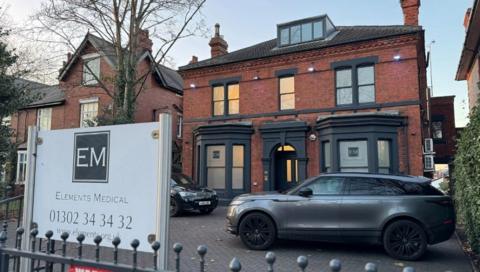 Elements Medical's clinic is a red-brick two-storey building with a room in the roof space. There is a small car park at the front and a sign saying "Elements Medical"