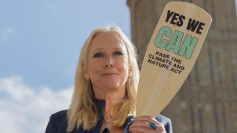 Dr Roz Savage in front of Big Ben holding a wooden oar that says: "Yes we can pass the climate and nature act".