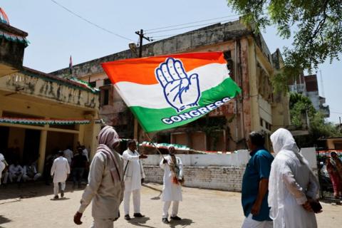 Man waves a large flag with the word "Congress" written on while several people walk past him