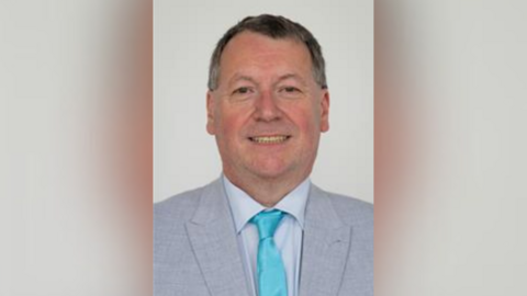 An image of a man in a suit wearing a turquoise tie.