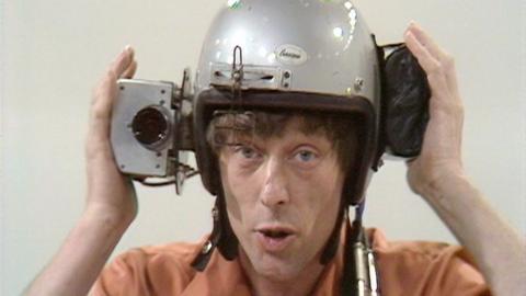 John Noakes demonstrating a helmet with a camera mounted to the side