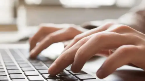 A generic image of a person typing on a computer keyboard. Both their hands are visible though the picture becomes more blurred in the background.