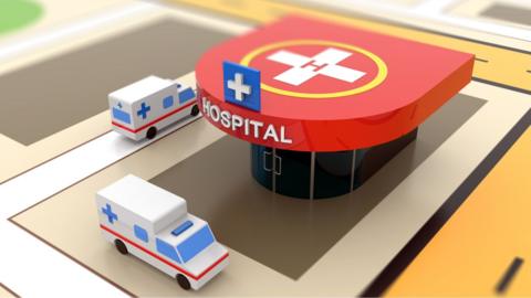 A photo of a model of a hospital with toy ambulances outside