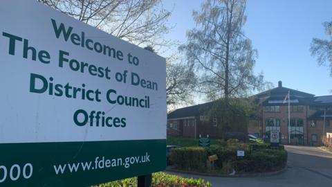 The sign for the Forest of Dean District Council Offices, with the council office behind it.