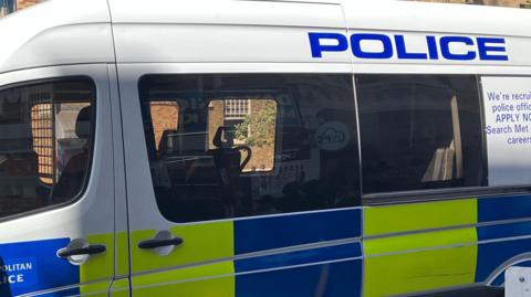 A Metropolitan Police van with a yellow and blue panel and the word Police and We're recruiting posted on the side.