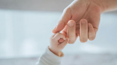 A small baby's hand holding the finger of a larger hand