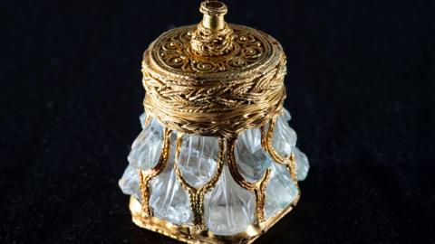 An image of a gold, crystal jar against a black background