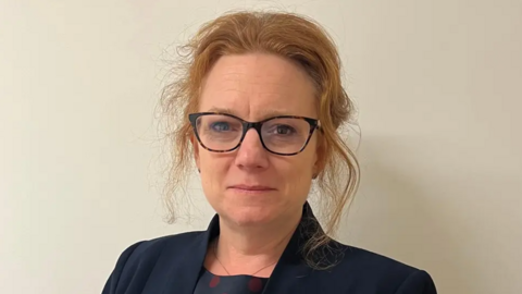 A woman with ginger hair wearing glasses looking into the camera