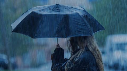 A woman holds a black umbrella in a torrential downpour.