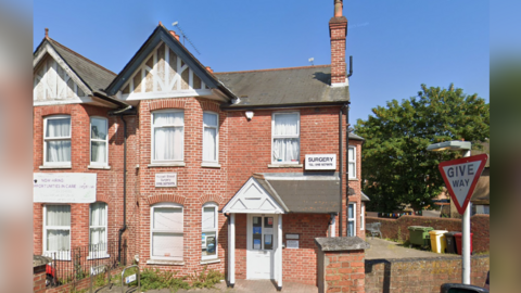 A Victorian semi-detached property on a main road. There is a sign on the building which says "surgery" and a phone number is below it.