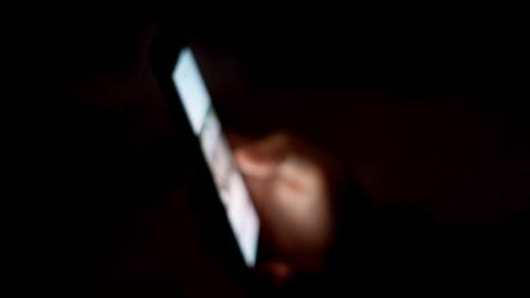 A smartphone display is lit up in a darkened room with the blurred image just visible of the hand holding it.