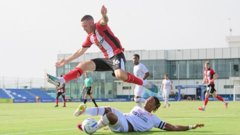 Lincoln City's Dom Jefferies jumps past Leyton Orient's Sean Clare as the latter puts in a tackle during their pre-season friendly in Spain on Friday.