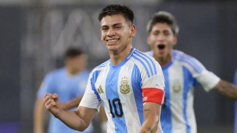 Claudio Echeverri wearing an Argentina football shirt holds up his fist