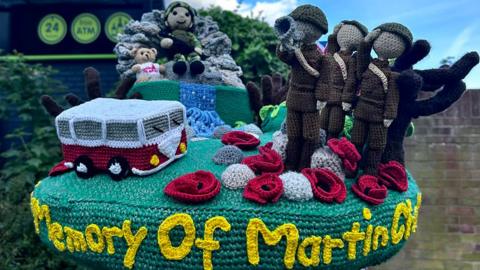 The postbox topper which has knitted soldiers, poppies and a red and white camper van with the words Memory of Martin Chadburn in yellow along the side