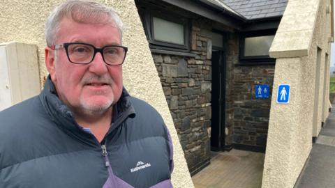 Councillor Hugh Hughes stands in front of public toilets in Borth, Ceredigion.