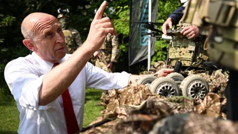 efence Secretary John Healey gestures to the drone in the sky as he views a screen showing it’s camera feed