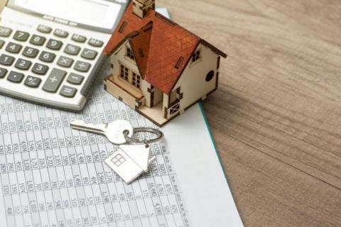 A set of keys, a calculator and a miniature model house set on top of a spreadsheet