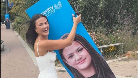 A woman in a white dress holding on to a blue cardboard cutout of her face
