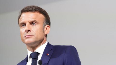 French President Emmanuel Macron wearing a blue suit with a stern look on his face