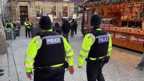 Two police officers in hi vis jackets pictured walking past stalls in Nottingham's Christmas market